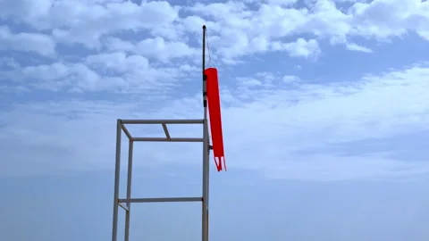 Red windsock hanging on a metal tower against a cloudy sky Видео 341292558