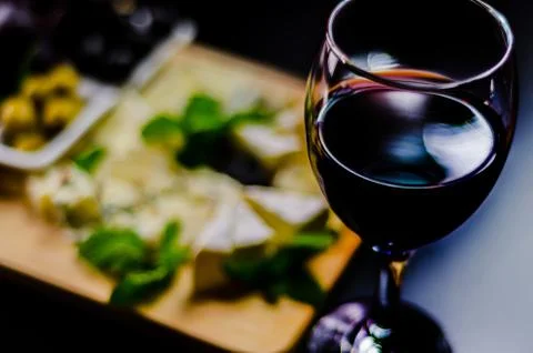 Red wine and set of different cheeses on a wooden board, delicious snack Stock Photos