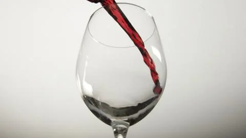 Red wine begins to pour into an empty wine glass Stock Photos