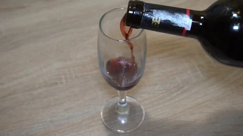 Red wine from a bottle is poured into a tall glass goblet. Stock Footage 123821673
