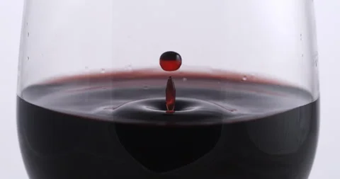 Red wine drop is falling with splashes in transparent glass in wine cellar Stock Footage 268801453