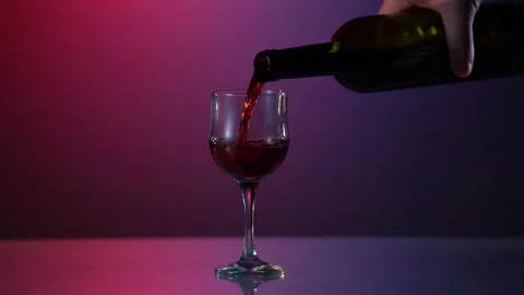 Red wine forms beautiful wave. Wine pouring in wine glass at red and blue Video stock 154579947