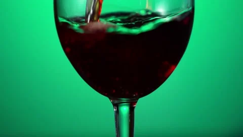 Red wine forms beautiful wave. Wine pouring in wine glass over green background Stock Footage 155642631