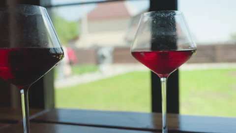 Red wine glasses by window with blurred view of people walking outside Video stock 316831058