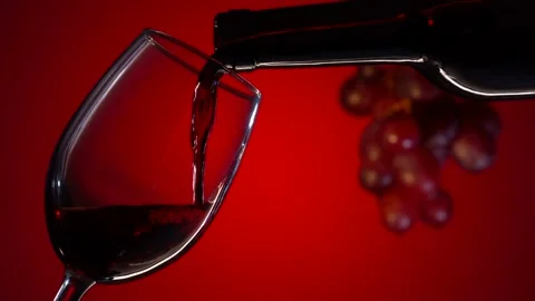 Red wine is poured into a glass from a bottle on a red background. Super Slow Stock Footage 153467775