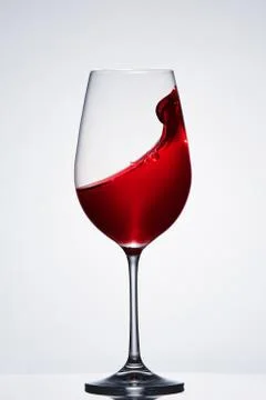 Red wine splash in the delicate elegant wineglass standing against light Stock Photos
