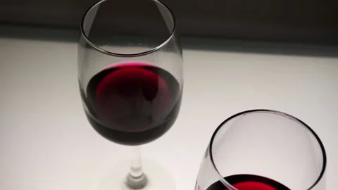 Red wine in two glasses on a light table. Slow motion, medium shot. Stock Footage 146640400
