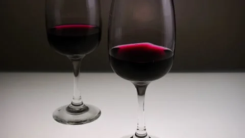 Red wine in two glasses on a light table. Slow motion, medium shot. Stock Footage 146640495