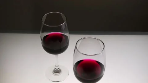 Red wine in two glasses on a light table. Slow motion, medium shot. Stock Footage 146640909