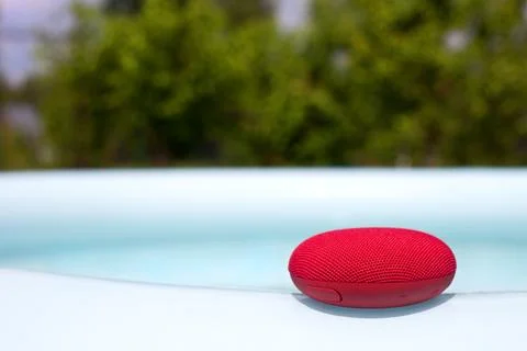Red wireless speaker lying around the pool. Stock Photos