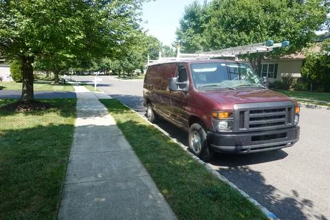 Red workman's van with ladders on top parked on a tree lined street Stock Photos