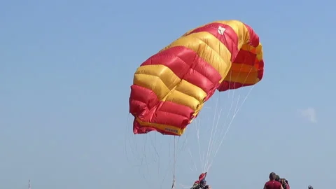 The red-yellow parachute forms against the background of the blue sky after the Stock Footage 95586325
