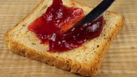 Redcurrant berry jam is spread with a knife onto a slice of multi-grain toast  Vídeo Stock 319872093