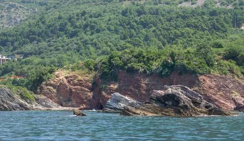 Reddish layered rock formations and coastal cliffs rising from the calm blue  Photos