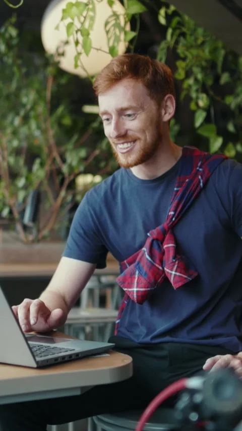 A redhaired man uses a tablet at a table, while another works on a laptop Stock Footage 301830303