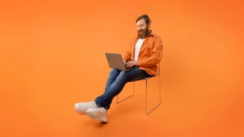 Redhaired programmer guy sits typing on his laptop, orange background 스톡 사진