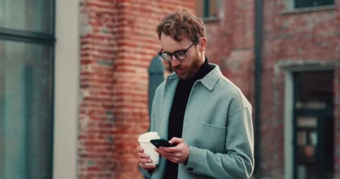 Redhead bearded guy using smartphone and holding coffee-to-go while walking. Stock Footage 240116295