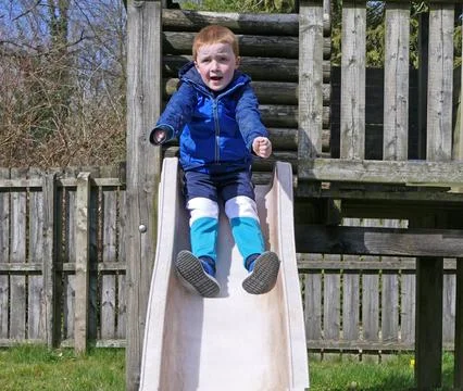 Redhead boy having fun playing on slides and swings at Playpark on a sunny da Fotos Stock