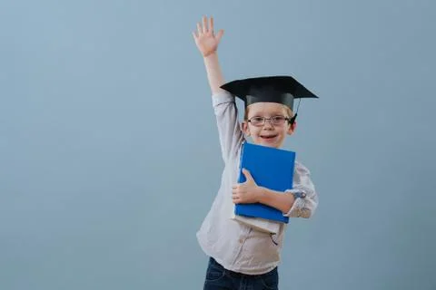 Redhead first grader boy in glasses and student hat raising his arm over blue Stock Photos