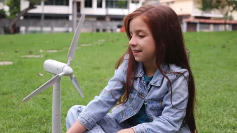 Redhead girl having fun with windmill turbine model on grass outdoor - Renewable Stock Footage 346192722