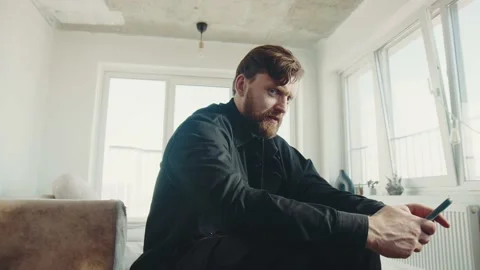 Redhead man with beard sitting at home and holding smartphone. 스톡 동영상 174716299