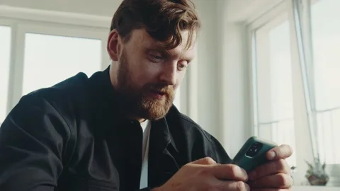 Redhead man with beard sitting at home and holding smartphone. 스톡 동영상 174716845