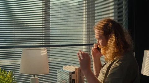 Redhead man talking on a mobile phone by a window with blinds Stock-Footage 339782911