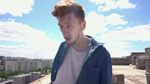 Redhead young man standing on the roof on background of the cityscape and blue Stock Footage