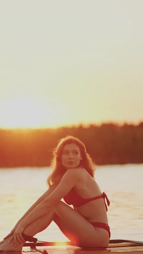 Redheaded woman in a red bikini posing on a paddleboard at sunset Stock Footage 341467903