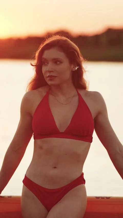 Redheaded woman in a red bikini posing on a paddleboard at sunset Stock Footage 341467944