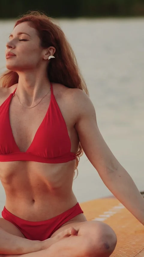 Redheaded woman in a red bikini posing on a paddleboard at sunset Stock Footage 341467989