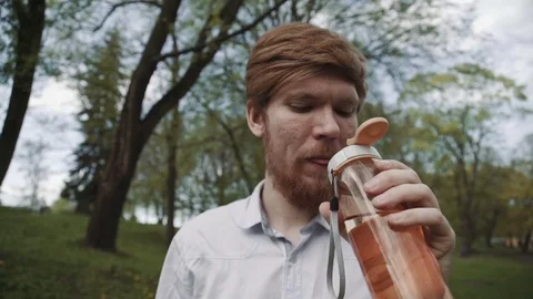 Redheaded young man with a beard drinking water from bottle. Cold drink summer Stock Footage 75899379