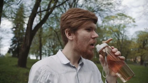 Redheaded young man with a beard drinking water from bottle. Cold drink summer Stock Footage 75899706