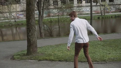 Redheaded young man with a beard foots starts ride on longboard in sunset park Stock Footage 75898202