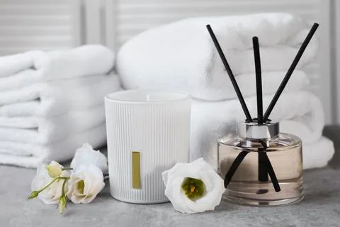 Reed diffuser, scented candle, flowers and folded towels on gray marble table Stock Photos