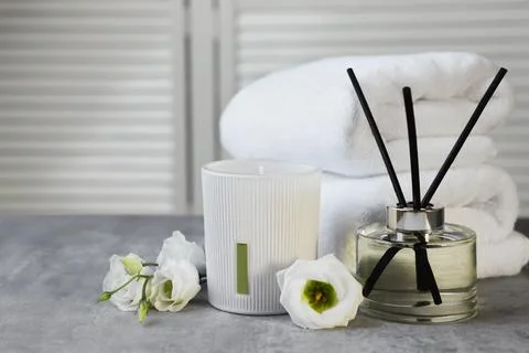 Reed diffuser, scented candle, flowers and folded towels on gray marble table Stock Photos