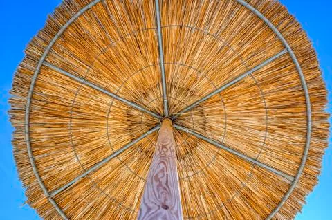 Reed umbrella with glowing sun at the empty beach in Asprovalt Stock Photos