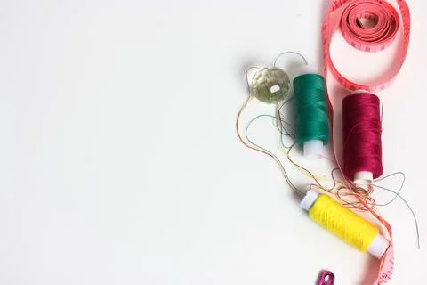 Reels of multicolored thread, measuring tape, and a pin on a white table flat Stock Photos