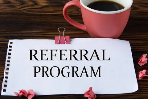 REFERRAL PROGRAM - words on a white sheet on a wooden brown background with a Stock Photos
