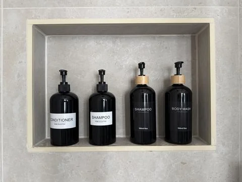 Refillable shampoo, conditioner and body wash pump bottles arranged in a built. Stock Photos