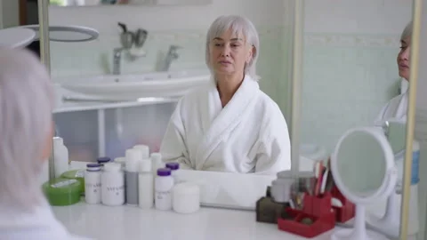 Reflection in bathroom mirror of gorgeous confident senior woman with grey hair Stock Footage 166089529