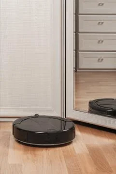 Reflection of black robot vacuum cleaner running before mirror in bedroom. mo Foto stock