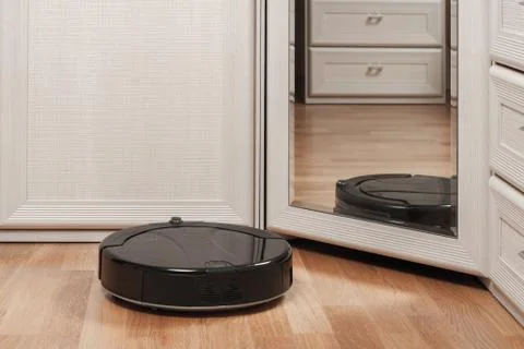 Reflection of black robotic vacuum cleaner running on laminate floor before m Foto stock