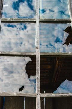 Reflection of blue sky and clouds in an old, broken window Stock Photos