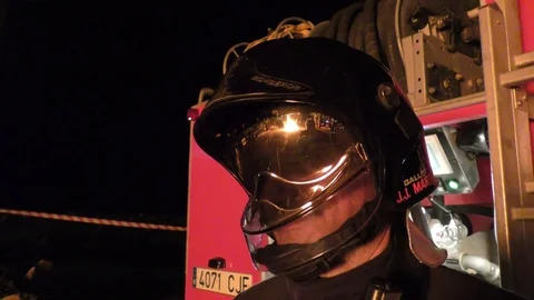 A reflection of a bonfire from the helmet of firefighter where he stands ready Видео 73447704