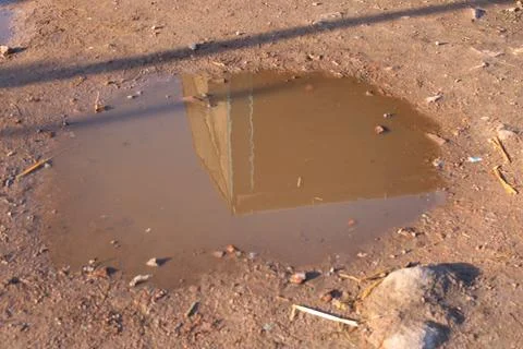 Reflection of a Building in a Small Muddy Puddle on Dirt Ground Fotos de archivo