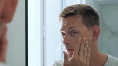 Reflection of Caucasian handsome young man applying moisturizing cream to face Stock Footage 256800504