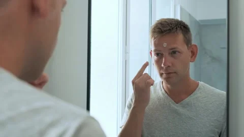 Reflection of Caucasian handsome young man applying moisturizing cream to face Stock Footage 270006978