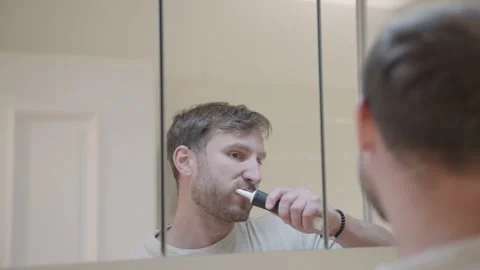 Reflection of a caucasian man using an electric toothbrush for his morning oral Stock Footage 335204577