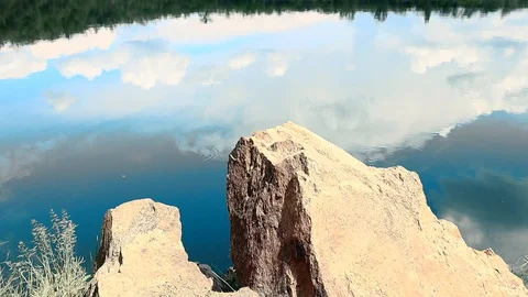 Reflection of clouds in a blue lake with large stones Stockbeeldmateriaal 129728380